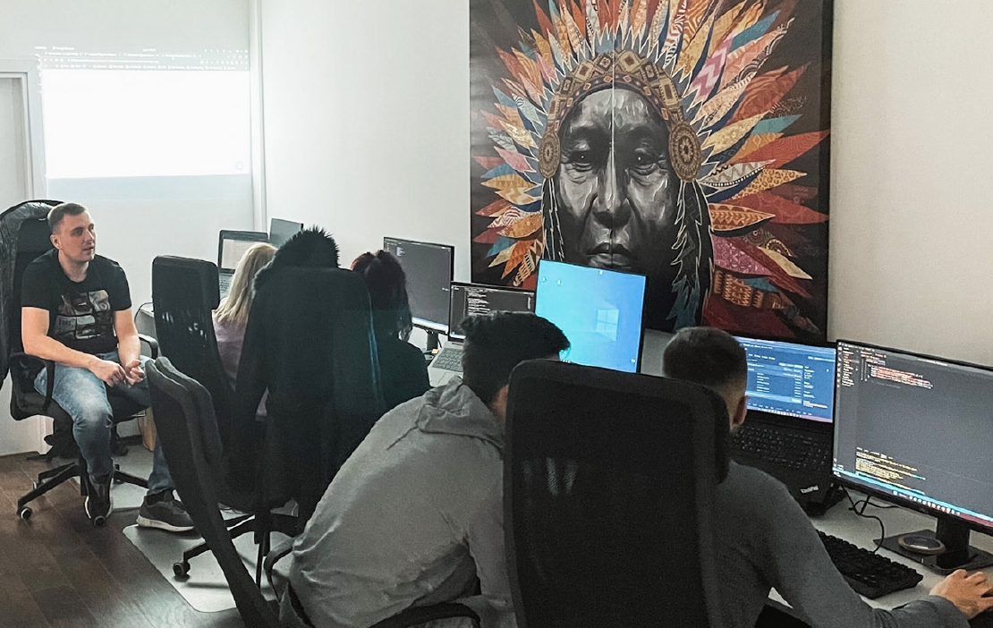 Developers writing code at a workshop in an office with big painting of a native american on the wall.