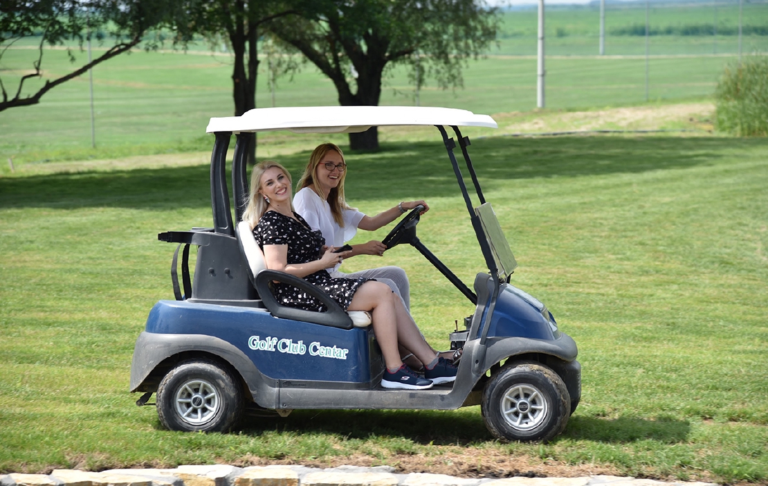 Two young women laughing and driving in a golf cart at a company event.