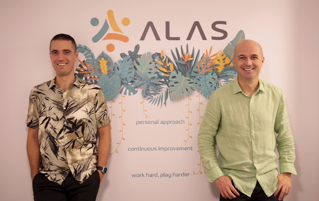 Co-founders Vilmos Somogyi and Tibor Dudjik standing in front of the new Alas logo and company values mural on the wall.